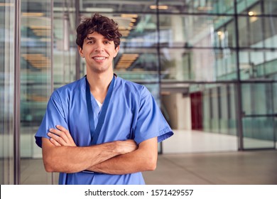 Portrait Of Young Male Doctor Wearing Scrubs Standing In Modern Hospital Building