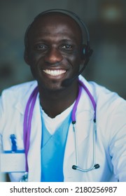 Portrait Of Young Male Doctor Wearing Headset While Using Computer At Desk In Clinic