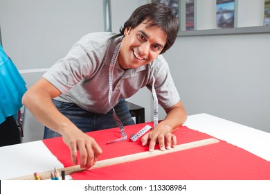 Portrait of young male dressmaker measuring a red fabric with ruler on table - Powered by Shutterstock