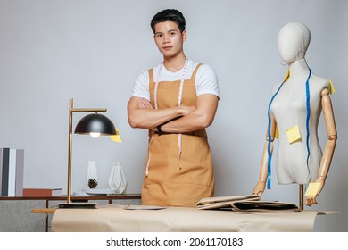 Portrait Young Male Fashion Designer Working With Fabric And Clothing Sketches At The Studio At Home, Full Of Tailoring Tools, Model And Equipment On Table