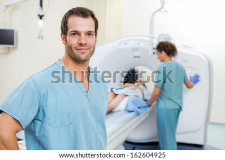 Portrait of young male nurse with colleague preparing patient for CT scan in hospital room