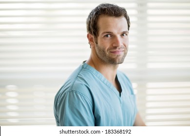 Portrait Of Young Male Nurse In Scrubs Smiling At Clinic