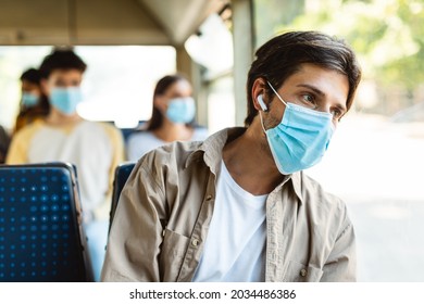 Portrait Of Young Male Passenger Wearing Medical Face Mask Traveling On Public Transit, Listening To Music In Wireless Headset Sitting And Looking Away At Window, Thinking, Going To Work By Bus