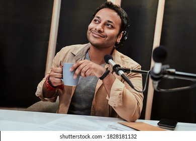 Portrait Of Young Male Radio Host In Headphones Waking Up, Drinking Coffee While Getting Ready For Broadcasting In Studio