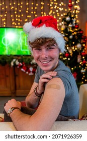 Portrait Of A Young Male Smiling After Getting A Vaccine - Man Showing Her Arm With Bandaid During A Christmas Party Dressing Red Cap