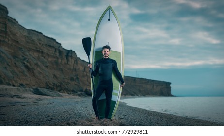 Portrait Of A Young Male Surfer In A Wetsuit On The Beach.