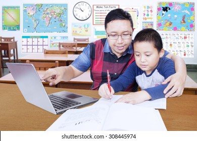 Portrait Of Young Male Teacher Helps His Student To Study With Laptop In The Classroom