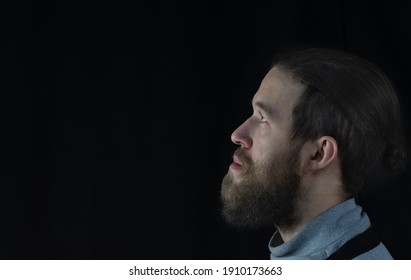 Portrait Of A Young Man With A Beard In Profile, Looking Up Against A Dark Background.