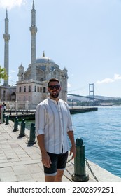 Portrait Of A Young Man With Beard And Sunglasses Posing In Front Of The Ortakoy Mosque And The Famous Bridge Of Istanbul.