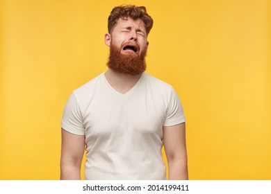 Portrait Of Young Man With Big Beard And Red Hair, Wears Blank T-shirt, Feels Depressed And Tired, Crying Like A Little Boy. Isolated Over Yellow Background.