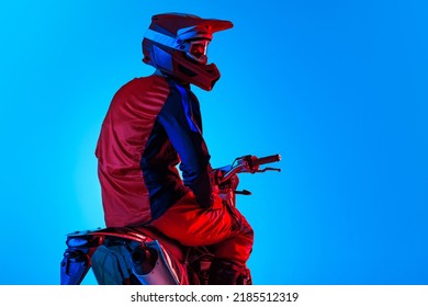 Portrait Of Young Man, Biker In Helmet Posing On Motorbike Isolated Over Blue Studio Background In Neon Light. Side View. Concept Of Motosport, Speed, Action, Hobby, Competition. Copy Space For Ad