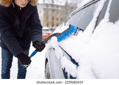 Portrait of young man cleaning snow off  car during winter snowfall. Transport, winter, weather, people and vehicle concept.