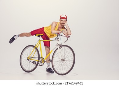 Portrait of young man in colorful clothes, uniform riding bike isolated over grey background. Flirty emotions. Concept of sport, hobby, work, active lifestyle, retro fashion. Copy space for ad