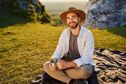 Portrait Of Young Man With Cup Sitting On Blanket In Mountains During Summer Hike In Jura Poland