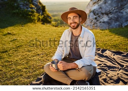 Portrait of young man with cup sitting on blanket in mountains during summer hike in Jura Poland