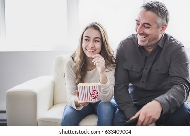 Portrait of a young man and daughter watching TV while eating popcorn on the sofa