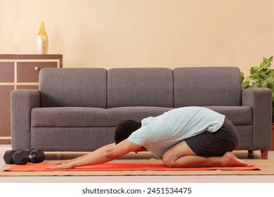 Portrait of a young man doing child pose yoga on exercise mat at home - Powered by Shutterstock