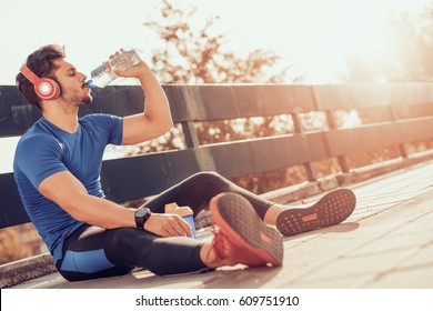 Portrait of young man drinking some water from a bottle while sitting and resting after training.