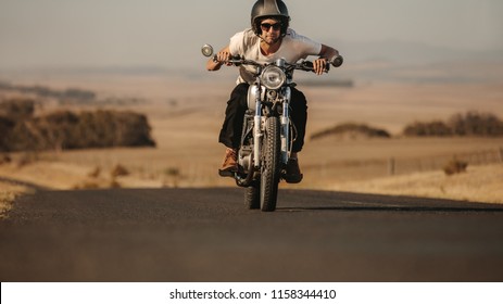 Portrait Of Young Man Driving A Motor Bike Fast On Country Highway. Male Rider Leaning Forward While Riding His Motorcycle.