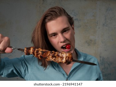 Portrait Of The Young Man Eating Meat On A Skewer With Cherry Tomato.