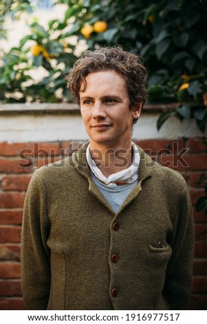 Portrait of a young man in the garden in front of a brick wall - Millennial dressed casually