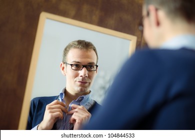 Portrait Of Young Man With Glasses Getting Ready, Dressing Up And Looking At Mirror