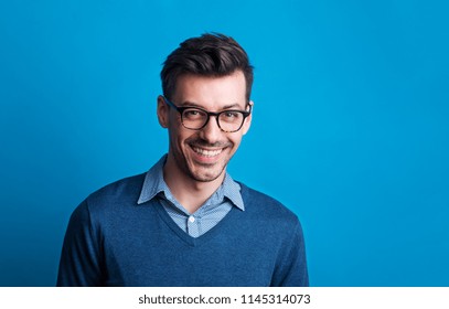 Portrait Of A Young Man With Glasses In A Studio On A Blue Background.