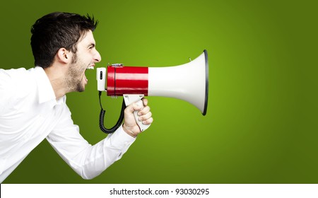 portrait of young man handsome shouting using megaphone over green background