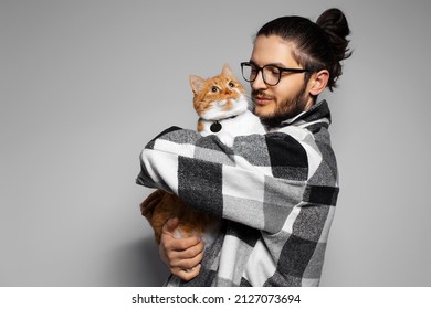 Portrait of young man holding in arms a cute red-white cat on grey background. - Powered by Shutterstock