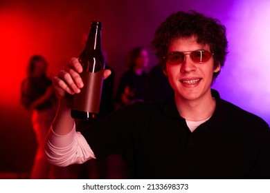 Portrait Of Young Man Holding Beer Bottle At Party And Smiling At Camera Lit By Neon Light