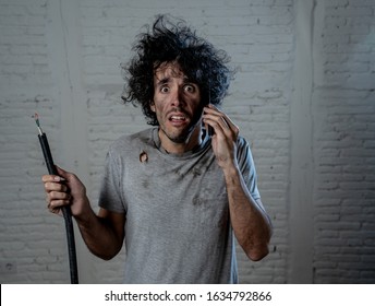 Portrait Of Young Man Holding Electrical Cable After Domestic Accident With Dirty Burnt Funny Face Expression Calling Desperate With Mobile Phone Asking For Help. Electricity Repairs And DIY Concept.