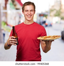 portrait of young man holding pizza and beer at street