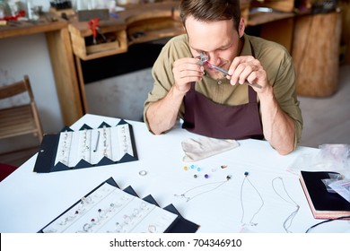 Portrait of young man inspecting jeweler with magnifying glass while appraising goods in pawn shop