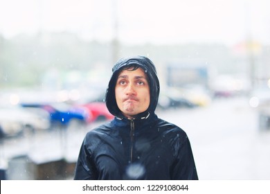 Portrait Of A Young Man In A Jacket With A Hood In The Rain On Blurred Background City Street, Close-up.