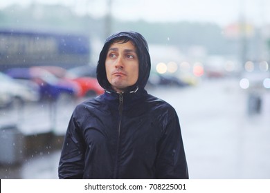 Portrait Of A Young Man In A Jacket With A Hood In The Rain On Blurred Background City Street, Close-up.