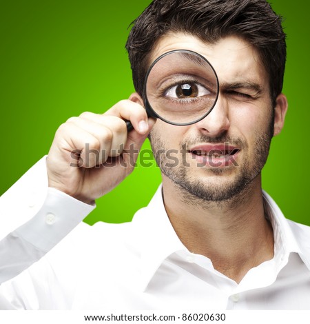 portrait of young man looking through a magnifying glass over green background