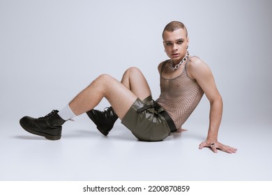 Portrait Of Young Man In Makeup, Smoky Eyes, Posing In String Vest And Shorts Isolated Over Grey Studio Background. Concept Of Fashion, Freedom Of Choice, Lifestyle, Lgbt, Generation Z, Trends