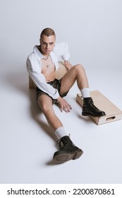 Portrait Of Young Man In Makeup, Smoky Eyes, Posing In Short Shirt And Leather Shorts Isolated Over Grey Studio Background. Concept Of Fashion, Freedom Of Choice, Lifestyle, Lgbt, Generation Z, Trends