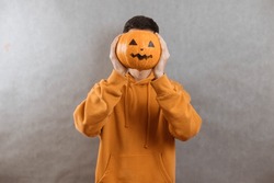 Portrait Of A Young Man On A Gray Background Covering His Face With A Pumpkin For Halloween. Copy Space.