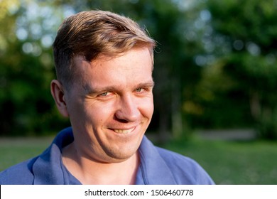 Portrait Of A Young Man On Nature Background. Emotion Facial Expression. Smug Smile, Feelings And People Reaction.