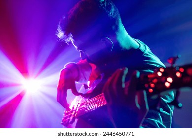 Portrait of young man performing playing chords electric guitar in neon light and visible smoke on stage. Rock and roll. Concept of rock and classic music, hobby and work, energy, music festivals. Ad - Powered by Shutterstock