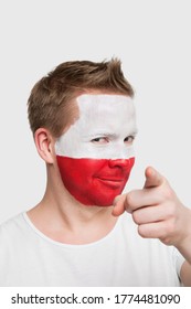 Portrait Of Young Man With Polish Flag Painted On Face Pointing Finger Against White Background