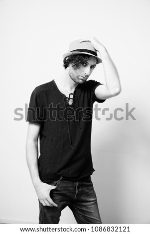 Portrait of young man posing as a model isolated on white background in studio. He’s  wearing a blue shirt, fedora trilby hat and looking at camera. Concept of confidence, introspection, sincerity.