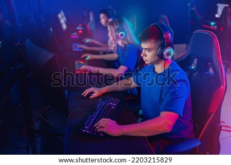 Portrait young man pro gamer with headphones playing in online video game in net cafe, neon color light, soft focus. Cybersport team concept.