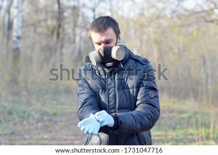 Portrait of young man in protective gas mask wears rubber disposable gloves outdoors in spring wood
