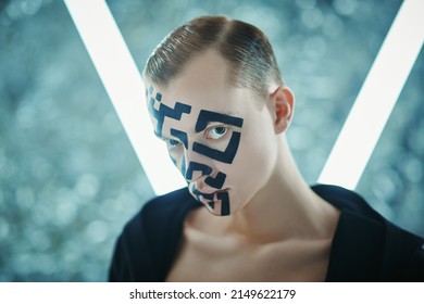 Portrait of a young man with a QR-code painted on his face standing in front of futuristic neon lamps and looking unfriendly at the camera. Modern technologies of human personification. 