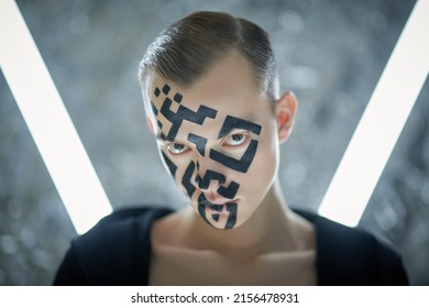 Portrait of a young man with a QR-code painted on his face standing in front of futuristic neon lamps and looking unfriendly at the camera. Modern technologies of human personification. 