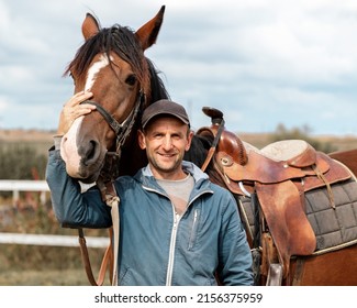 Portrait of a young man rider with brown horse next to wooden fencing - Shutterstock ID 2156375959