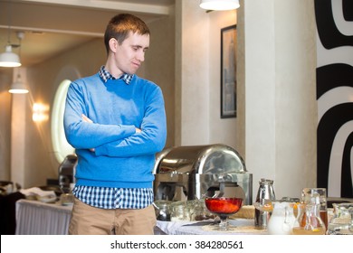 Portrait Of Young Man At Self-catering Breakfast In Hotel Restaurant, Picky Eater Fed-up With Food, Showing Disappointment On His Face