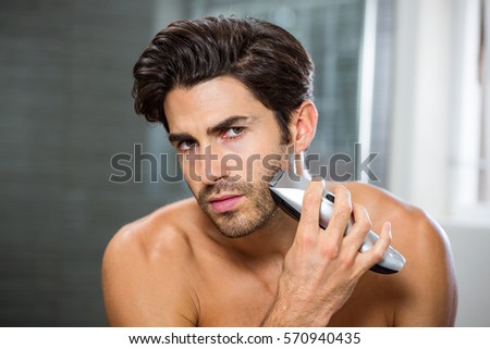 Portrait of young man shaving with trimmer